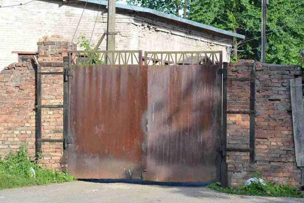 Rusty metal driveway gate misaligned and no longer closing properly at a residential property